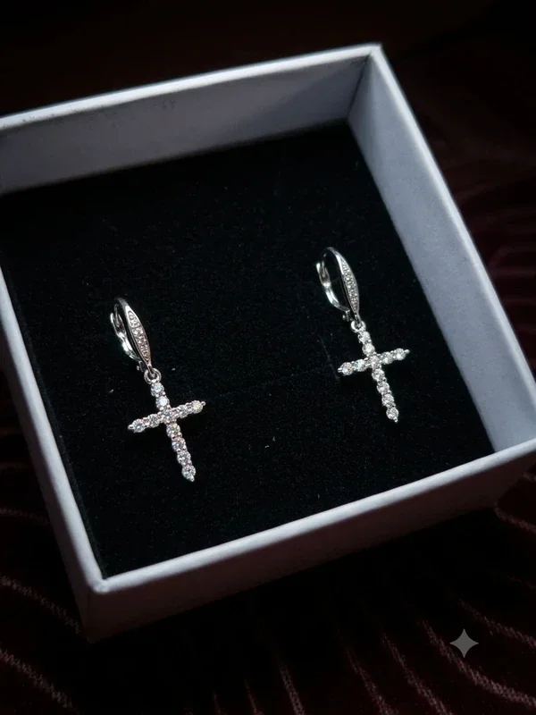 Pendientes de cruz plateados con piedras en una caja oscura
